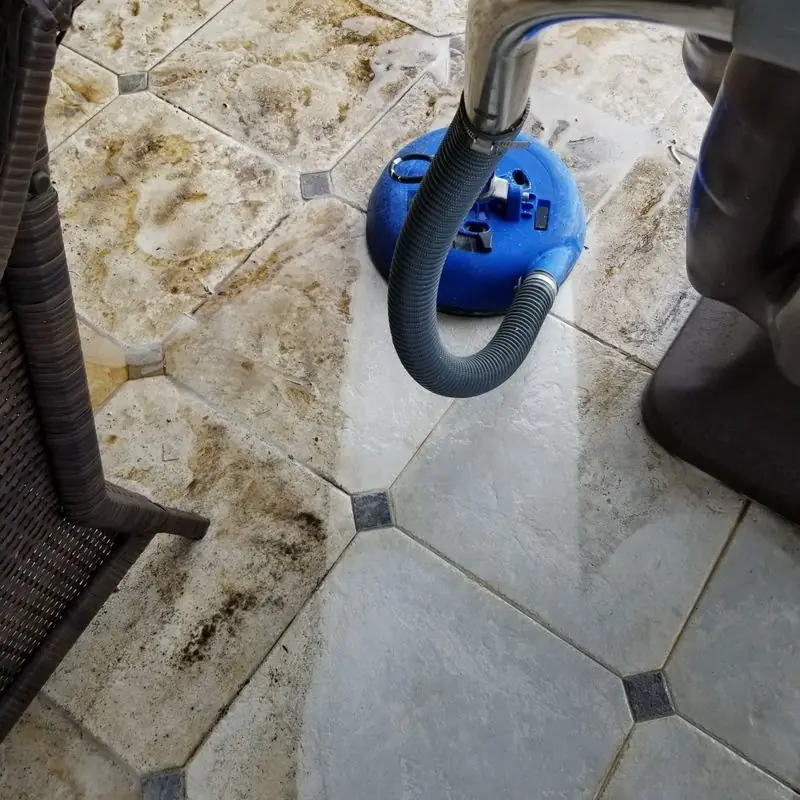 Hex patio tile with the cleaned half beside grout still dark with grime, blue extraction tool on the tile
