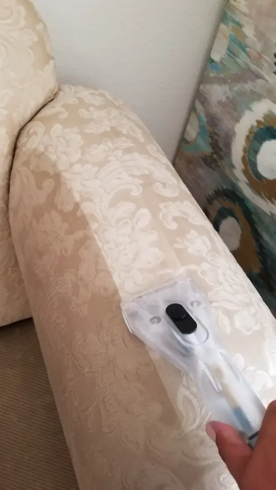 Upholstery steam tool working along the arm of a cream damask chair